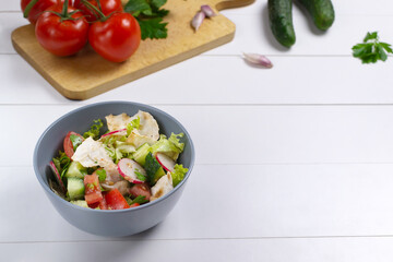 Fattoush salad in a gray bowl with ingredients on a white background. Copy space. Levantine fattoush bread salad, which is prepared from dried pita bread  with the addition of  vegetables and herbs. 