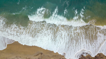 Obraz na płótnie Canvas Aerial view of beautiful waves crashing on the sand creating foam, Greece