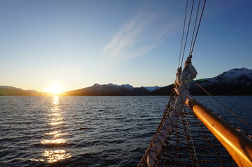 Sunrise in a Norwegian fjord called Kaldfjord with a sailing mast and sail in the foreground.
