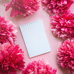 A blank paper notebook on a pink background surrounded by delicate beautiful flowers of peonies