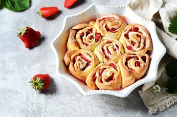Homemade bun rolls with strawberries in a baking dish on a gray background