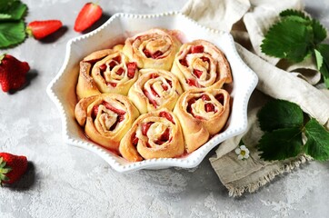 Homemade bun rolls with strawberries in a baking dish on a gray background