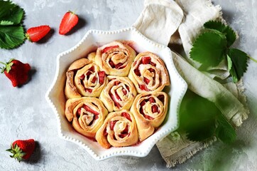 Homemade bun rolls with strawberries in a baking dish on a gray background
