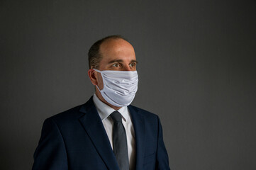 portrait of a smart dressed business man with suit and tie and protective face mask looks into the distance off camera. Concept of hope for businesses and enterprises after corona epidemic