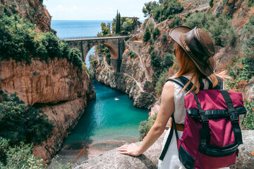 A girl in a cowboy hat with a backpack enjoys an incredibly beautiful view of a stone bridge over...