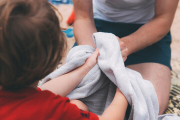 Obraz na płótnie Canvas Father's day. Dad and son. Dad wipes his son's hands with a towel on the beach. Happy family father and child. Hands of a young man and his son blurred in the foreground from back. After washing hands