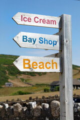 Fototapeta premium Sign post giving directions to the gift shop and beach in Rhossili village. Blue sky background in a vertical format.