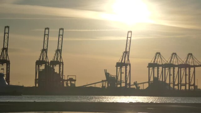 Shimmering sunset golden hour river water with British harbour port cranes silhouettes skyline