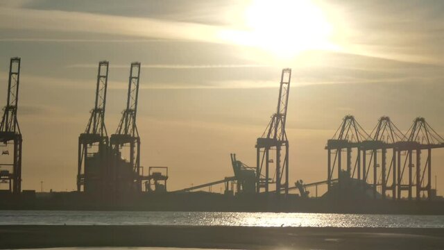 Shimmering sunset golden river water with British harbour cargo shipyard cranes silhouettes skyline