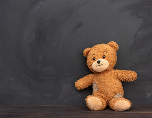 brown teddy bear sits on a brown wooden table, behind an empty black chalk board