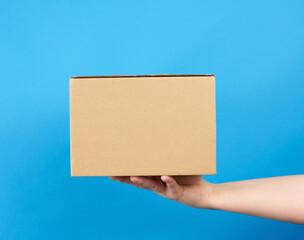 hand holds a brown cardboard box of paper on a blue background