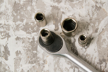 Old wrench with a rattle and different nozzles on a background of gray putty