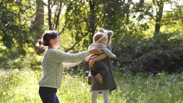 Mother and elder sister spin and walk with baby toddler making first steps on park grass happy family girls play together on nature
