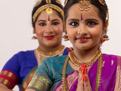  Young bharatnatyam dancer standing ahead of her teacher with her hands folded. 
