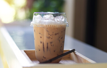 Iced milk tea in plastic glass, put on the wooden floor, behind it is a green garden.