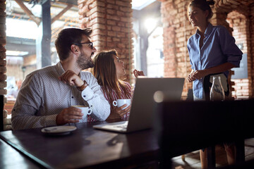 young couple explaining to a waitress what they want to order in cafe with laptop in front of them.