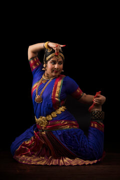 Bharatnatyam dancer in trinetra pose during her performance on a dark background. 
