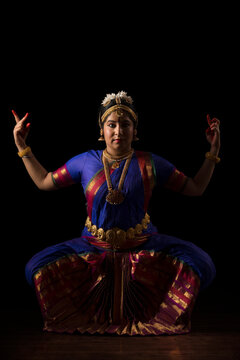 Bharatnatyam dancer in a devi pose during her performance on a dark background. 
