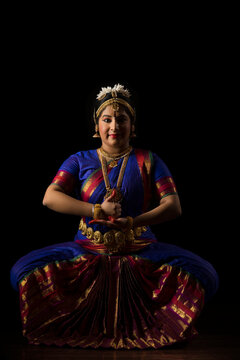 Bharatnatyam dancer in a shiva lingam pose during her performance on a dark background. 
