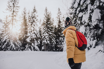 young man with yellow coat, red backpack and wool cap in a snowy mountain landscape