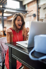 delighted  female watching content on her laptop with headphones in ears and fists up in YES position