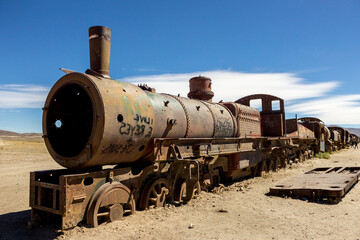 Fototapeta na wymiar Uyuni rusty train railway cemetery. Train graveyard. Old abandoned trains and wheel sets on sand in middle desert. Landscape view in Uyuni. Tourist Attraction In Bolivia. Nature Of South America
