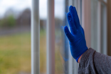Women hand with medical gloves next to the window indoor. Home isolation. Corona virus. Stay at home.