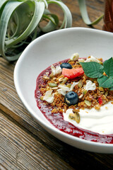 Sweet and healthy breakfast - granola with yogurt, raspberry jam and summer fruits in a bowl on a wooden background