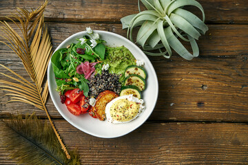 Superfood - a bowl of quinoa, fried cheese, guacamole, poached poached egg and cherry tomatoes on a wooden background