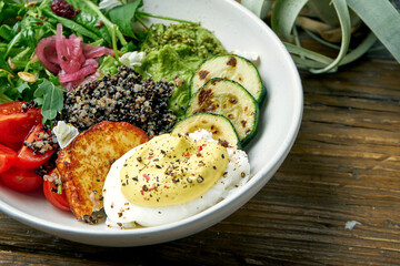 Superfood - a bowl of quinoa, fried cheese, guacamole, poached poached egg and cherry tomatoes on a wooden background