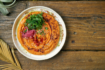 Classic oriental appetizer - baked peppers hummus with greens and arugula in a white plate on a wooden background