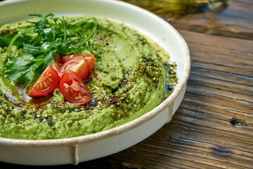 Classical oriental appetizer - avocado hummus with greens and cherry tomatoes in a white plate on a wooden background