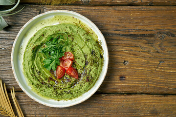 Classical oriental appetizer - avocado hummus with greens and cherry tomatoes in a white plate on a wooden background