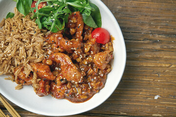 Asian dish - chicken in sweet and sour sauce with rice and arugula salad in a bowl on a wooden background. Street food