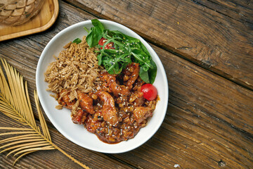 Asian dish - chicken in sweet and sour sauce with rice and arugula salad in a bowl on a wooden background. Street food