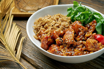 Asian dish - chicken in sweet and sour sauce with rice and arugula salad in a bowl on a wooden background. Street food