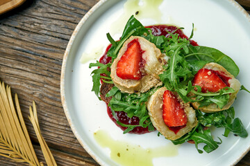 Appetizing toast with goat cheese, red jam, arugula and strawberries with rye bread on a plate on a wooden background