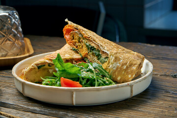 Vegetarian shawarma roll with spinach, tomatoes, hummus and melted cheese in a plate on a wooden background