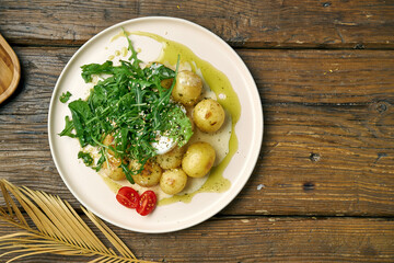 Boiled, young potatoes with arugula salad and poached egg seasoned with cream sauce on a wooden background