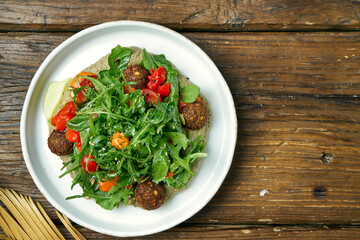 Appetizing vegetarian salad with arugula, falafel, cherry tomatoes and hummus on a wooden background