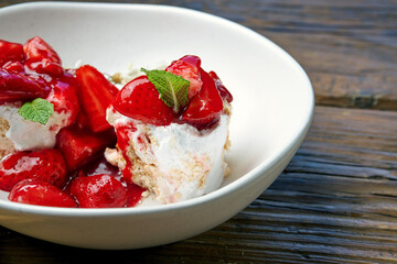 Airy cakes with white cream, strawberries, jam in a white bowl on a wooden background. Dessert Anna Pavlova