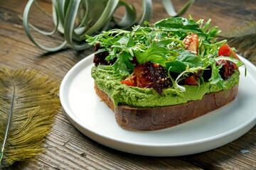 Trend street food - avocado toast with guacamole, arugula and tofu cheese in a white plate on a wooden background. Vegetarian food