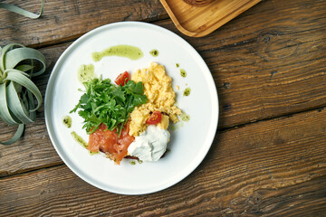 Appetizing breakfast - scramble eggs, with arugula, salmon and toast with Greek yogurt in a plate on a wooden background