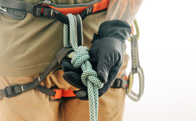 Man climber in harness holding rope knot eight, close-up.