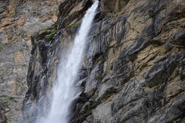 Stunning landscape at roaring Vasudhara falls, people enjoying the fall, big rocky mountains and clouds. Monsoon trek taken in August starts near Mana (last indian village) in Uttarakhand India.