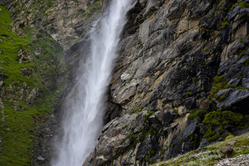 Stunning landscape at roaring Vasudhara falls, people enjoying the fall, big rocky mountains and clouds. Monsoon trek taken in August starts near Mana (last indian village) in Uttarakhand India.