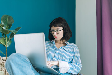 Beautiful brunette with a short haircut works in the home office on a blue background. Typing on a laptop, calling on the phone, transferring documents, making notes, drinking coffee from a mug.