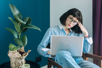 Beautiful brunette with a short haircut works in the home office on a blue background. Typing on a laptop, calling on the phone, transferring documents, making notes, drinking coffee from a mug.