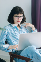 Beautiful brunette with a short haircut works in the home office on a blue background. Typing on a laptop, calling on the phone, transferring documents, making notes, drinking coffee from a mug.