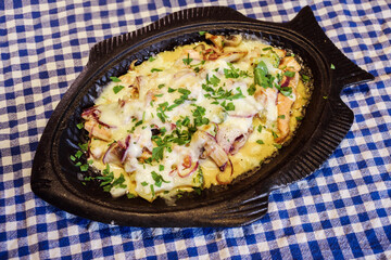 Delicious fried fish with cheese, mushrooms, onion served in the fish-shape plate on the white and blue towel. Traditional Mediterranean, greece, italian or french meal.